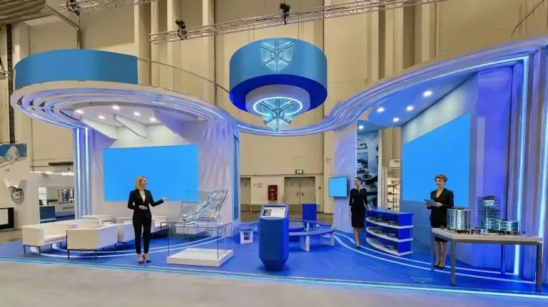 Azafatas Glasstec Düsseldorf 2026 dando la bienvenida a los visitantes dentro de un stand dedicado a tecnologías de procesamiento de vidrio.